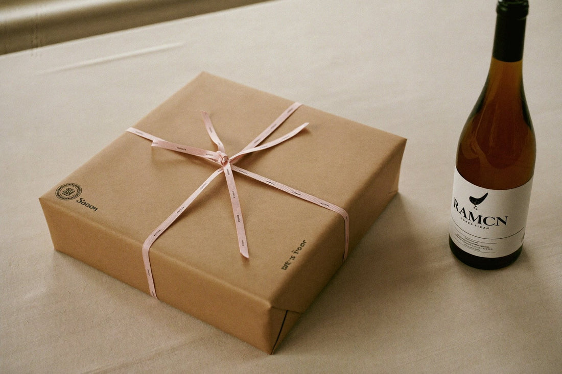 Ingepakt cadeau met lint naast een fles witte wijn